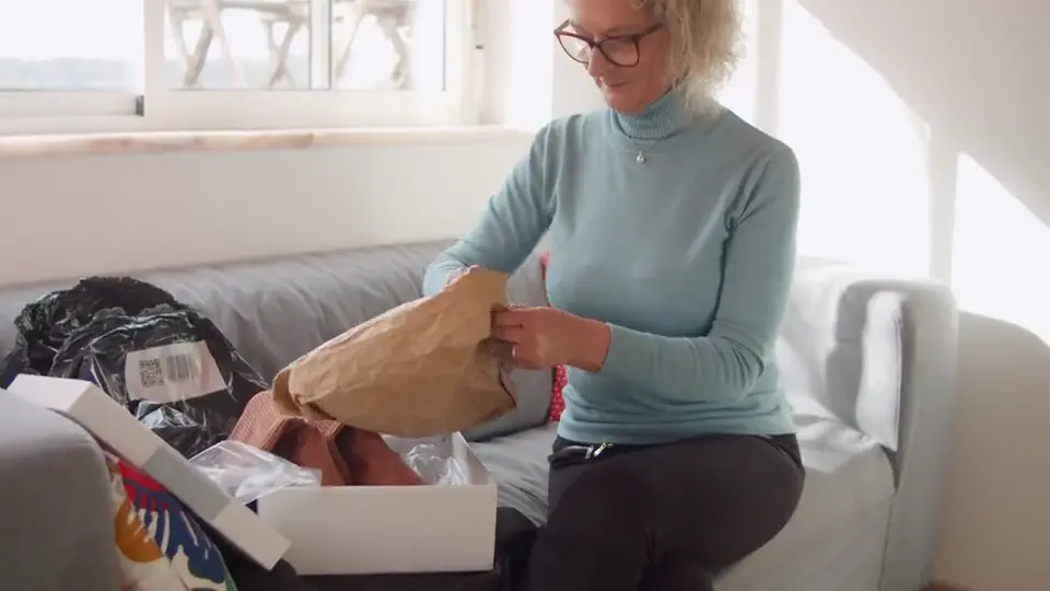 Une femme sourit en ouvrant un colis chez elle